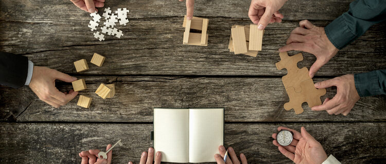 Eight businessmen planning a strategy in business advancement each holding  different but equally important metaphorical element - compass,  puzzle pieces, pegs, cubes, key and one making notes.